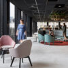 Modern office lounge area featuring sleek, low-profile Rix armchairs with a minimalist design. The Australian-made Rix chair with timber legs, feature a shell made from recycled post-consumer plastic and a 4-leg base crafted from American Oak. The chair is upholstered in two-tone fabric, with the seat in Instyle Chunky and the shell in Kvadrat Raas. The setting is accentuated by a large window in the background, allowing natural light to flood the space.