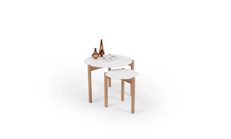 A small round stool placed next to a wooden table with a book and a pair of scissors on top, against a white background.