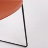 Close-up of a modern chair with an orange seat and a black metal frame against a white background.