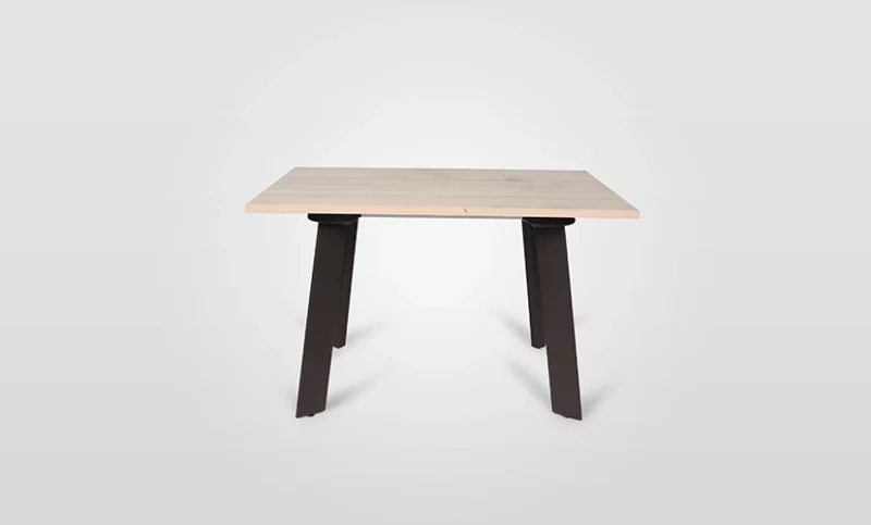 A simple wooden table with a light-colored top and angled black legs on a plain background.