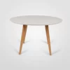 A modern round table with a white top and wooden legs on a white background.