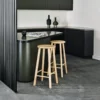 A modern kitchen interior featuring a small black counter with two Australian Made wooden Met stools, contemporary furniture from Australia, minimalist black decor items, and sleek cabinetry in neutral tones.