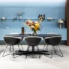 Contemporary dining room featuring Australian-inspired furniture, including a sleek black table and four gray chairs, accented by a vase of flowers. Blue cabinetry and decor gracefully adorn open shelves in the background.